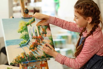 Pretty female pupil studying of classic art at work place. Creativity little red haired girl with...