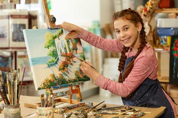 Positivity little red haired girl with braid smiling at camera and showing her colorful hand made...