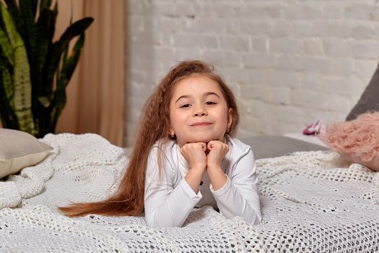 A happy litle girl lies on the bed in the room