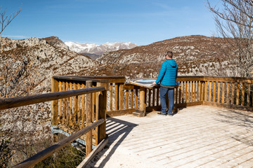Hombre joven disfrutando las vistas de unas montañas nevadas desde un mirador voladizo. Pirineos,...