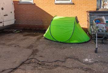 Small green tent used by a homeless person and set up in an alleyway.