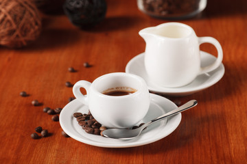 White espresso coffee Cup, coffee beans and milk jug on wooden background. Concept of coffee breaks and serving coffee