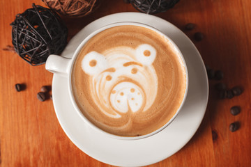 Cappuccino coffee with latte art in the form of bear close-up on a wooden table. The concept of coffee in the cafe