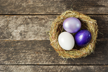 Bright purple colored Easter eggs in nest on wooden background, selective focus image. Happy Easter card