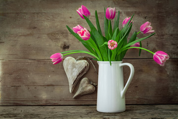 Ländlicher Blumenstrauß aus pinken Tulpen in weißer Vase auf Holzregal