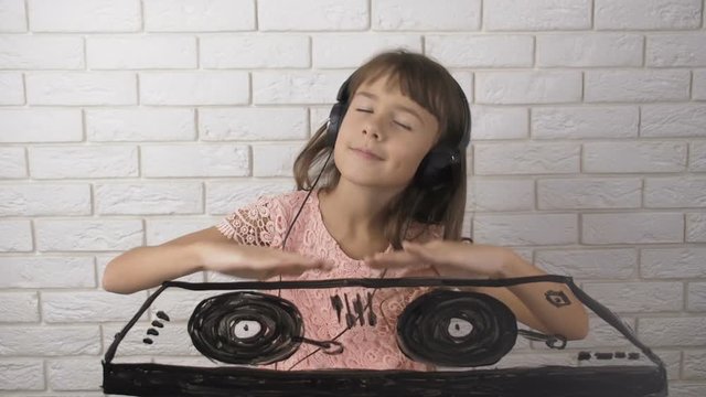 A child creates music. A cute girl in headphones plays a DJ.