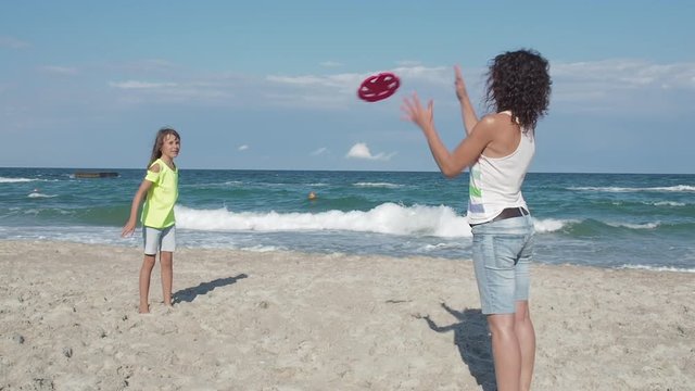 Family playing at a resort. Having fun on vacation. Mother and daughter play frisbee on the beach.