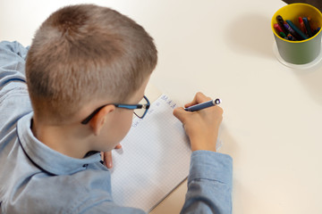 Chłopiec uczy się pisać litery. Dłonie chłopca  trzymają długopis. Pisanie liter w zeszycie. - obrazy, fototapety, plakaty