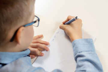 Nauka pisania. Chłopiec siedzi przy biurku i uczy się pisać litery długopisem w zeszycie. - obrazy, fototapety, plakaty