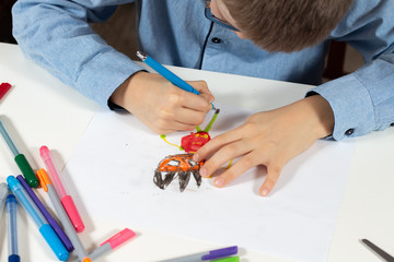 Naklejka premium Dłonie dziecka trzymają długopis i rysują wymyśloną postać na białej kartce papieru.