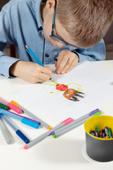 Dłonie dziecka trzymają długopis i rysują wymyśloną postać na białej kartce papieru. - obrazy, fototapety, plakaty