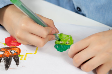 Dłonie dziecka trzymają zielony flamaster i rysują zielonego ludzika na białej kartce papieru.