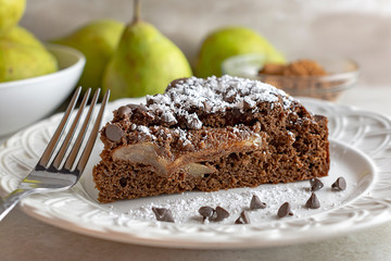 Close up side view of Chocolate Pear Cake sprinkled with powdered sugar.  Fork and chocolate chips...