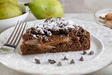 Close up view of chocolate pear cake.  Chocolate chips, powdered sugar and fork on plate.
