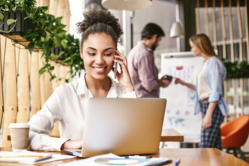 The strength of the team is each individual member. The strength of each member is the team. Beautiful young woman is talking by telephone while working in creative office