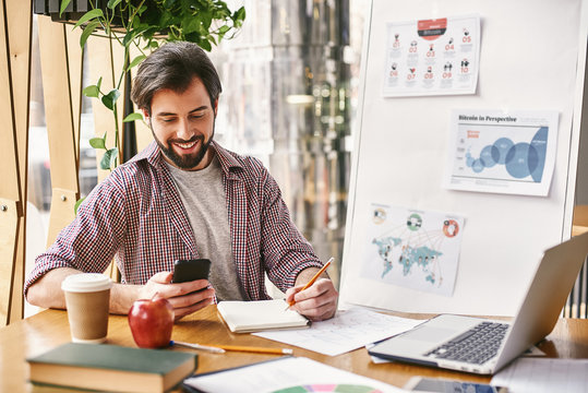 Success usually comes to those who are too busy to be looking for it. Smiling manager sitting in office and looking on his phone