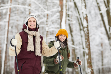 Waist up portrait of happy active couple skiing in forest and looking at camera enjoying winter,...