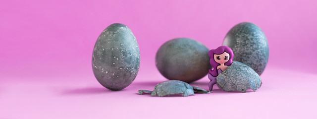 Three gray, blue Easter eggs, like stones. Two toy mermaids.