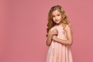 Little girl with a blond curly hair, in a pink dress is posing with a candy