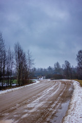 Empty Countryside Landscape in Cloudy Winter Day with Snow Partly Covering the Ground and Fog, Puddles and Tire Marks on the Road