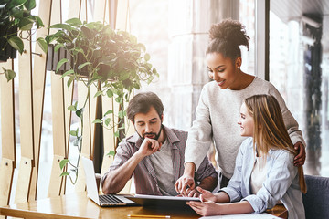 Happy multiracial millennial colleagues discussing company financial statistics at briefing in office, employees brainstorming analyzing growing sales, developing success strategies, reading reports - Powered by Adobe