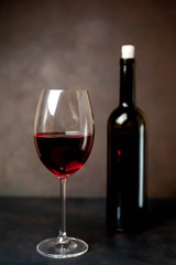 Wine glass with red wine and bottle against a stone background.