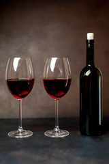 Glasses with red wine and a bottle on a stone background.