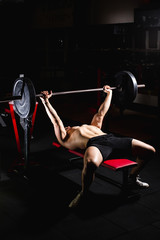 Fototapeta na wymiar Sporty brutal strong guy doing exercises with a barbell in the gym. Brutal sports man. Bodybuilder in training in the gym. Health and fitness