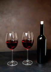 Glasses with red wine and a bottle on a stone background.
