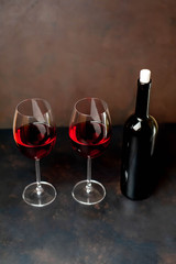 Glasses with red wine and a bottle on a stone background.