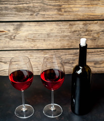 glasses with red wine and a bottle on a background of stone and wood