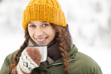 Head and shoulders portrait of pretty young woman drinking hot cocoa outdoors and looking at camera...