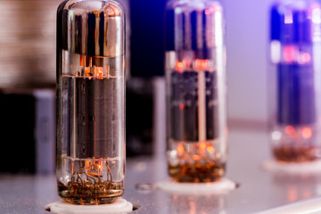 Old-fashioned electronic device amplifier with glowing bulb diode lamp for sound reproduction,...