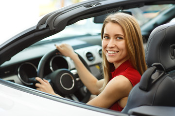 Fototapeta na wymiar Female customer testing new comfortable cabriolet before buying. Young beautiful redhaired woman sitting white automobile, smiling, looking at camera and posing in auto showroom.