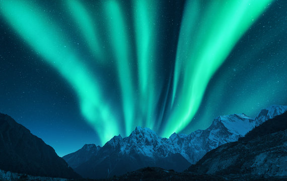 Aurora borealis above snow covered mountain range in europe. Northern lights in winter. Night landscape with green polar lights and snowy mountains. Starry sky with aurora. Nature background. Space