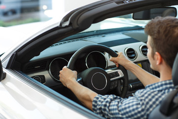 Back view of male customer sitting on seat of driver in automobile, keeping hands on wheel and...