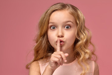 Naklejka premium Little girl with a blond curly hair, in a pink dress is posing for the camera