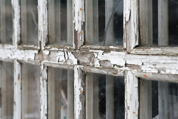 Cracked white wooden frame of an old window with peeling paint and rotten wood