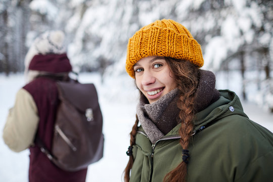 Portrait of active young woman looking at camera during winter hike with boyfriend in background, copy space