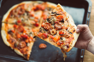 Piece of pizza held in the hands of a woman. Home made pizza served by hand. A snack at a home...