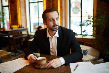 Portrait of handsome businessman drinking coffee in cafe during break and looking away pensively, copy space