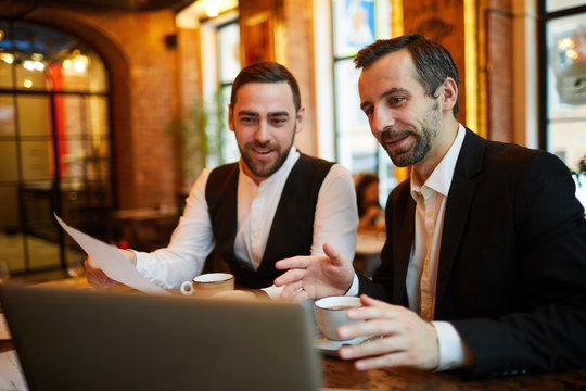 Portrait of two cheerful business people using laptop in cafe while working at coffee break, copy space