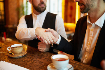 Close up of two unrecognizable business people shaking hands during meeting in cafe, copy space