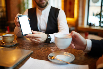 Fototapeta premium Closeup of unrecognizable businessman showing smartphone with blank screen during meeting in cafe, copy space