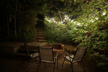 Beautiful backyard lighting strung through trees surrounded by patio furniture and a fire pit 