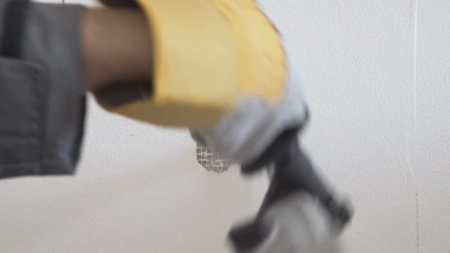Builder Worker With Electric Rotary Hammer brush plate makes a hole in the wall, closeup