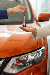 Dealer giving key to new owner at orange jeep on background.