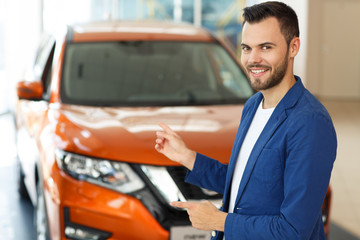 Bearded man pointing by hand at orange jeep behind him.