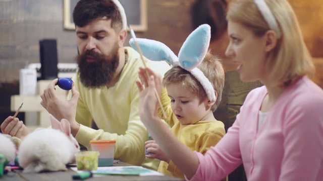 Mother, father and son are painting eggs. Happy family are preparing for Easter. Happy easter. Cute little child boy wearing bunny ears. Happy family smiling and laughing, drawing on eggs.