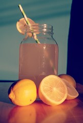 Drink in Mason jar with half lemons, paper stripped straw and blue background